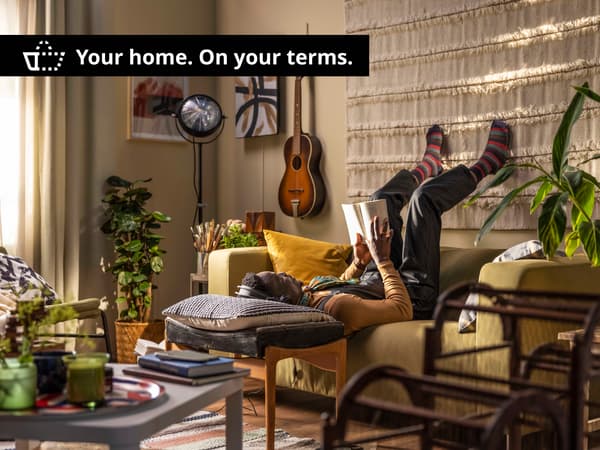 A person laying on a yellow sofa upside down and reading a book, his head on a pillow resting on a coffee table. A black bar at the top of the image with white text saying "Your home. On your terms."