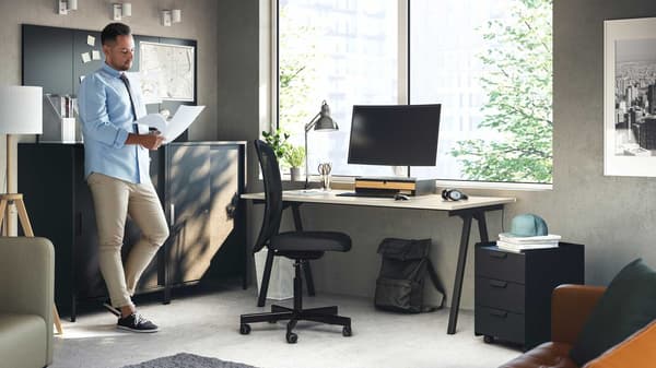 A person leaning on a cabinet reads some documents
