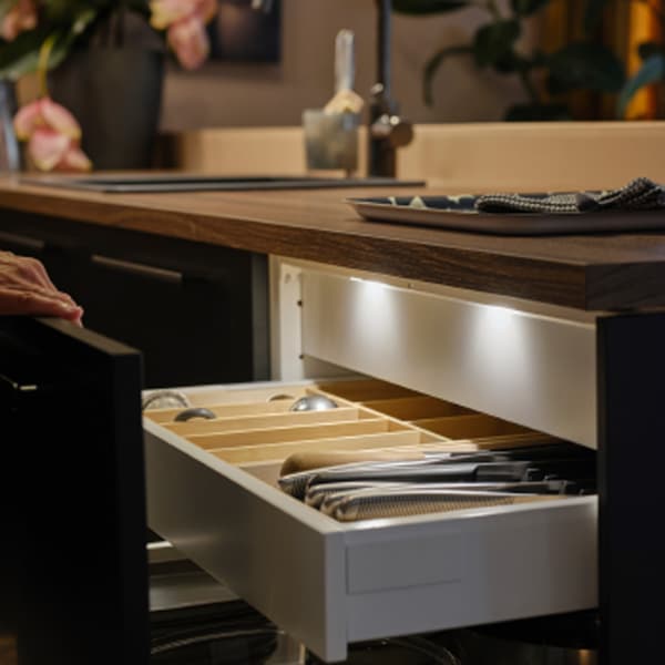A person opens a kitchen drawer with a matt anthracite front, showing MITTLED LED kitchen drawer lighting with sensor inside.