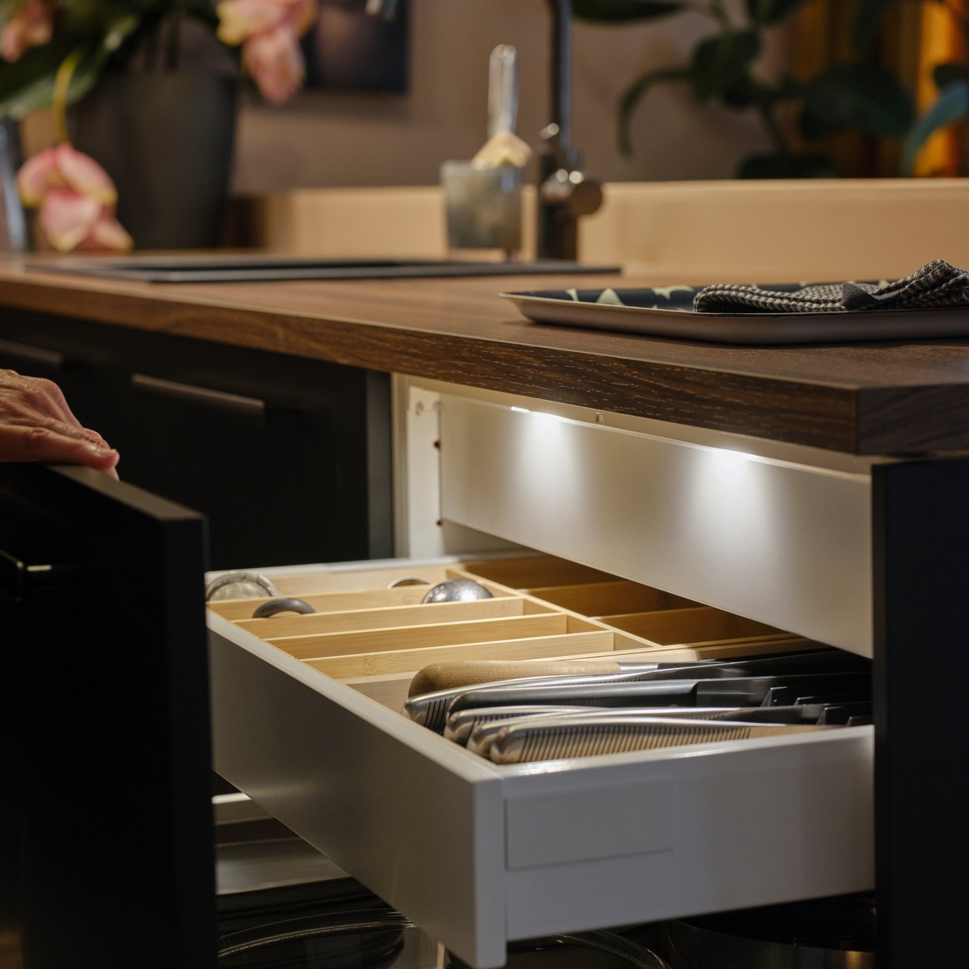 A person opens a kitchen drawer with a matt anthracite front, showing MITTLED LED kitchen drawer lighting with sensor inside.