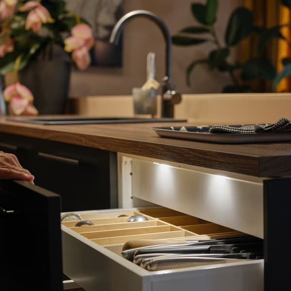 A person opens a kitchen drawer with a matt anthracite front, showing MITTLED LED kitchen drawer lighting with sensor inside.