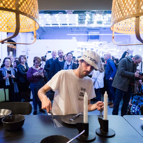 A person playing crockery like an instrument on a black table top, with crowds watching.