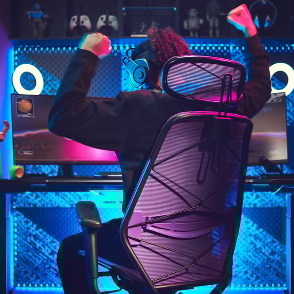 A person playing video games on a gaming desk and chair, the wall lit up with blue neon lights.