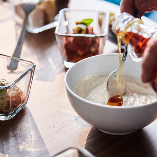A person pooring oil into a white bowl with other ingridents.