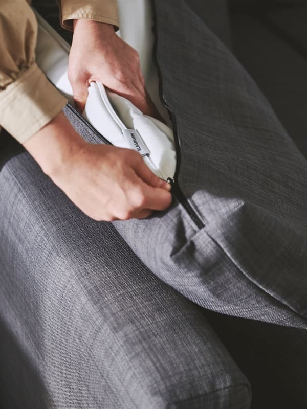 A person puts in VIMLE sofa cushion in a dark grey cover.