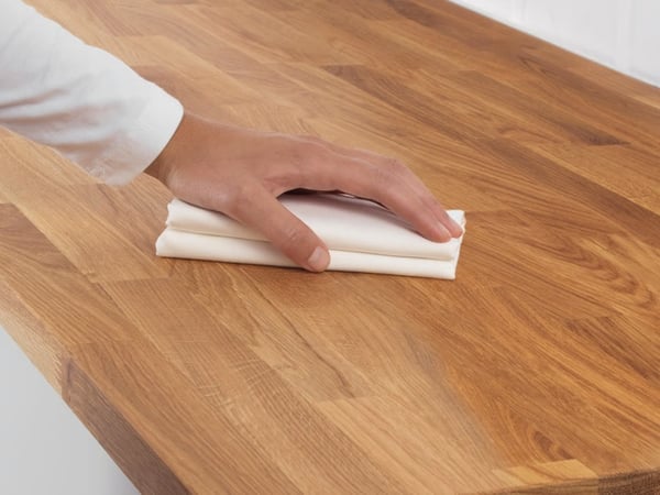 A person rubbing oil into a wooden countertop using a folded cloth.