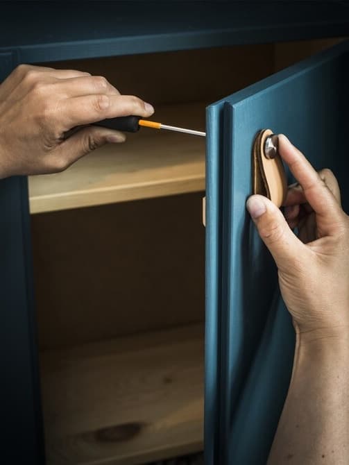 A person screwing in a leather handle in a IVAR unit door. 