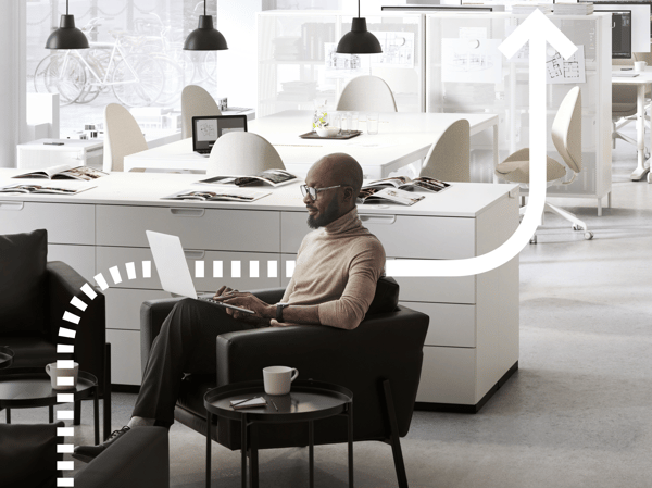 A person sits at a desk and works on a computer. We see a cellphone next to the person. The background shows more computers.