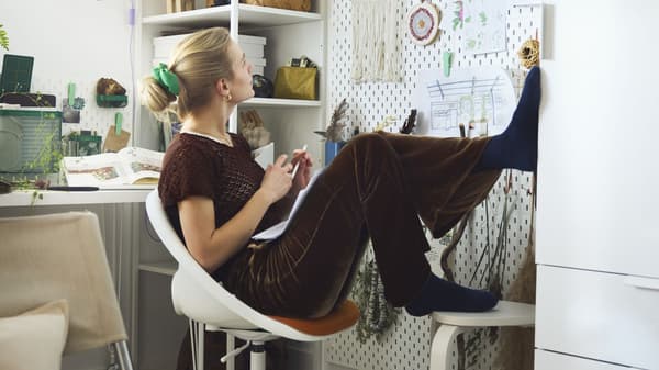 A person sitting at a desk with their feet up and staring at a bulletin board in front of them. 