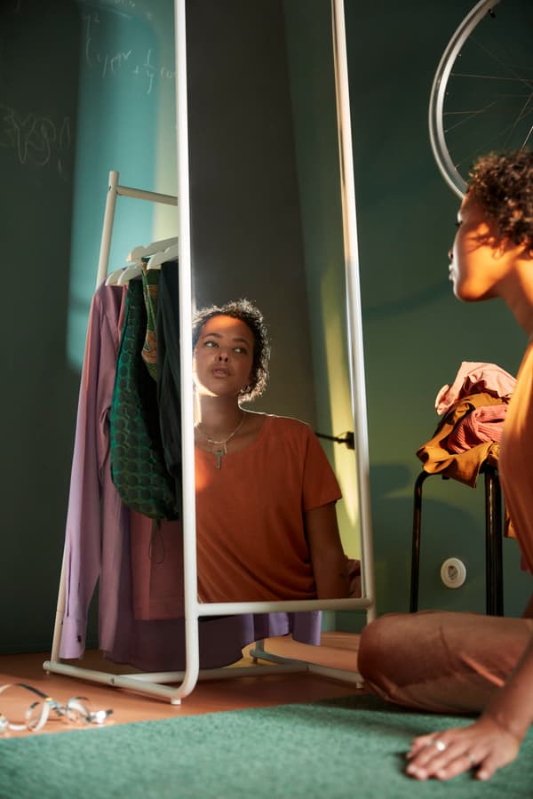 A person sitting in front of a white standing mirror in a green room.