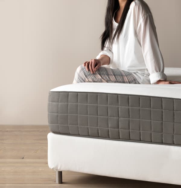 A person sitting on a grey and white mattress on a white bedframe.