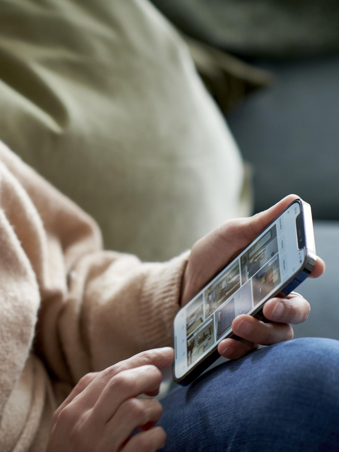 A person sitting on a sofa, browsing images for inspiration on their smartphone.