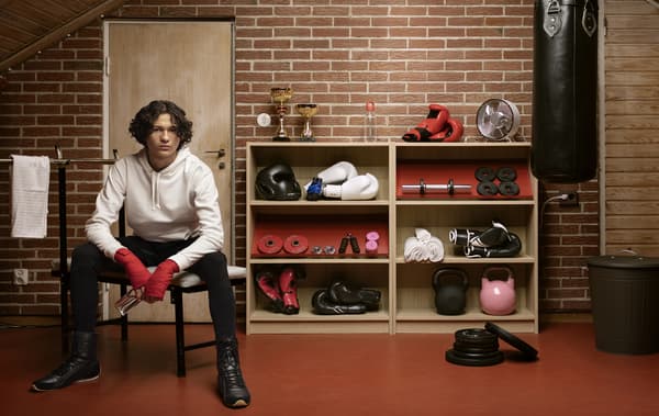A person sitting on a stool next to two bookcases containing sports equipment.