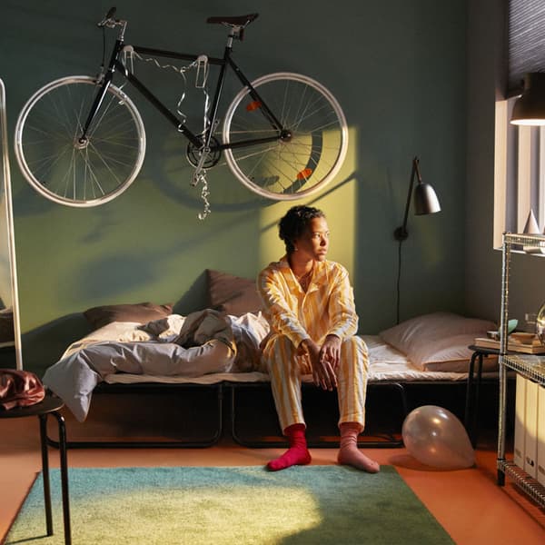 A person sitting on the HAMMARN futon in a green bedroom.