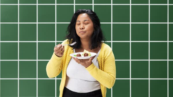 A person standing, eating a plate of meatballs