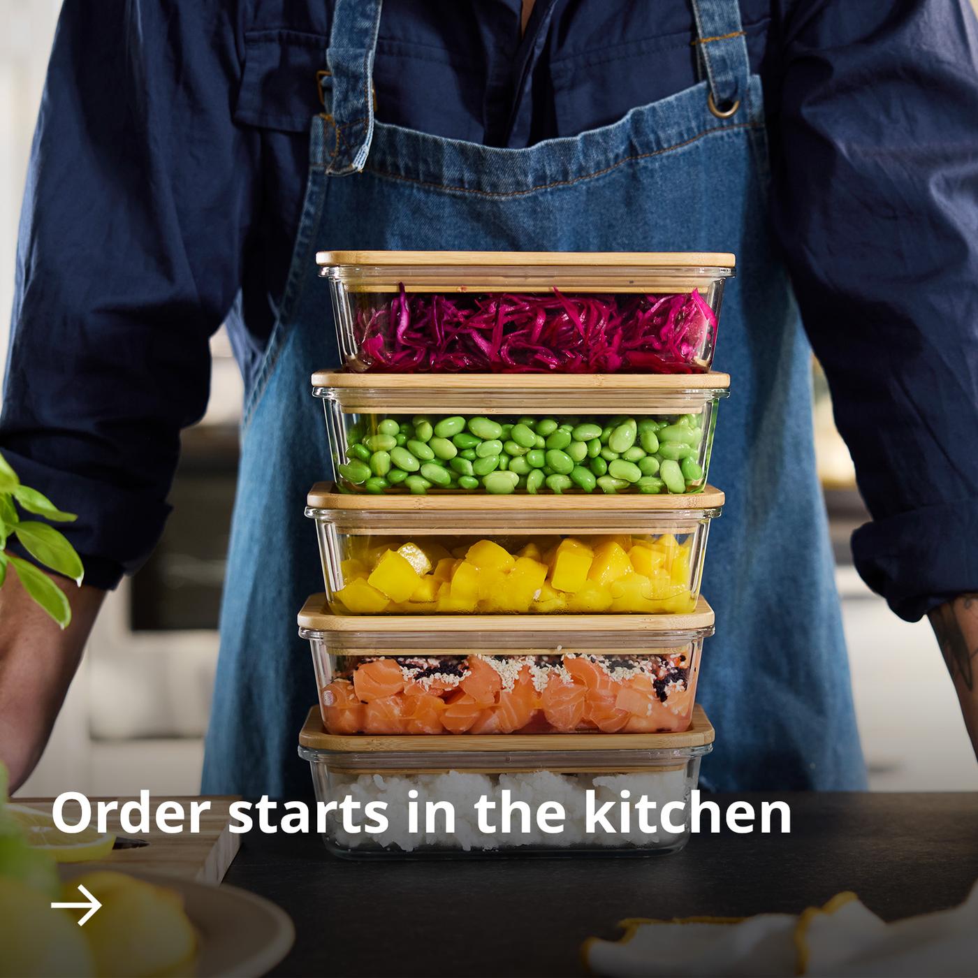 A person standing in front of a stack of colourful IKEA 365+ food containers filled with different ingredients and meals.