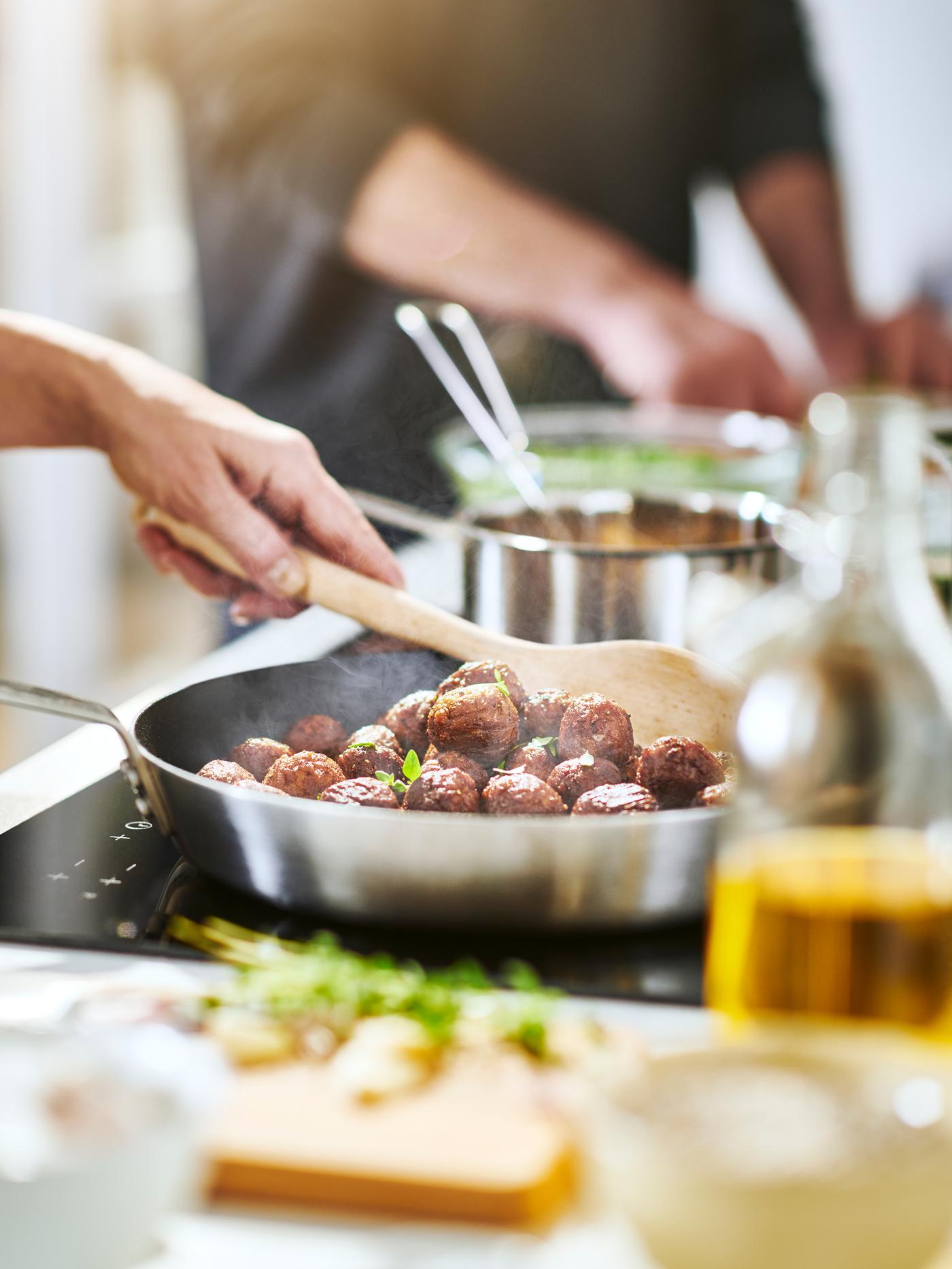 A person stirring HUVUDROLL plant balls with a wooden spoon whilst they’re being fried on an induction hub.