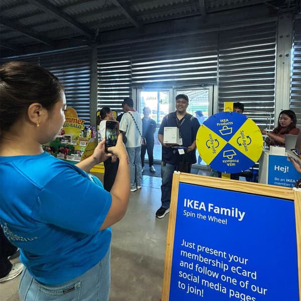 A person takes a photo at an IKEA event with a spinning wheel promoting membership perks, surrounded by other attendees.