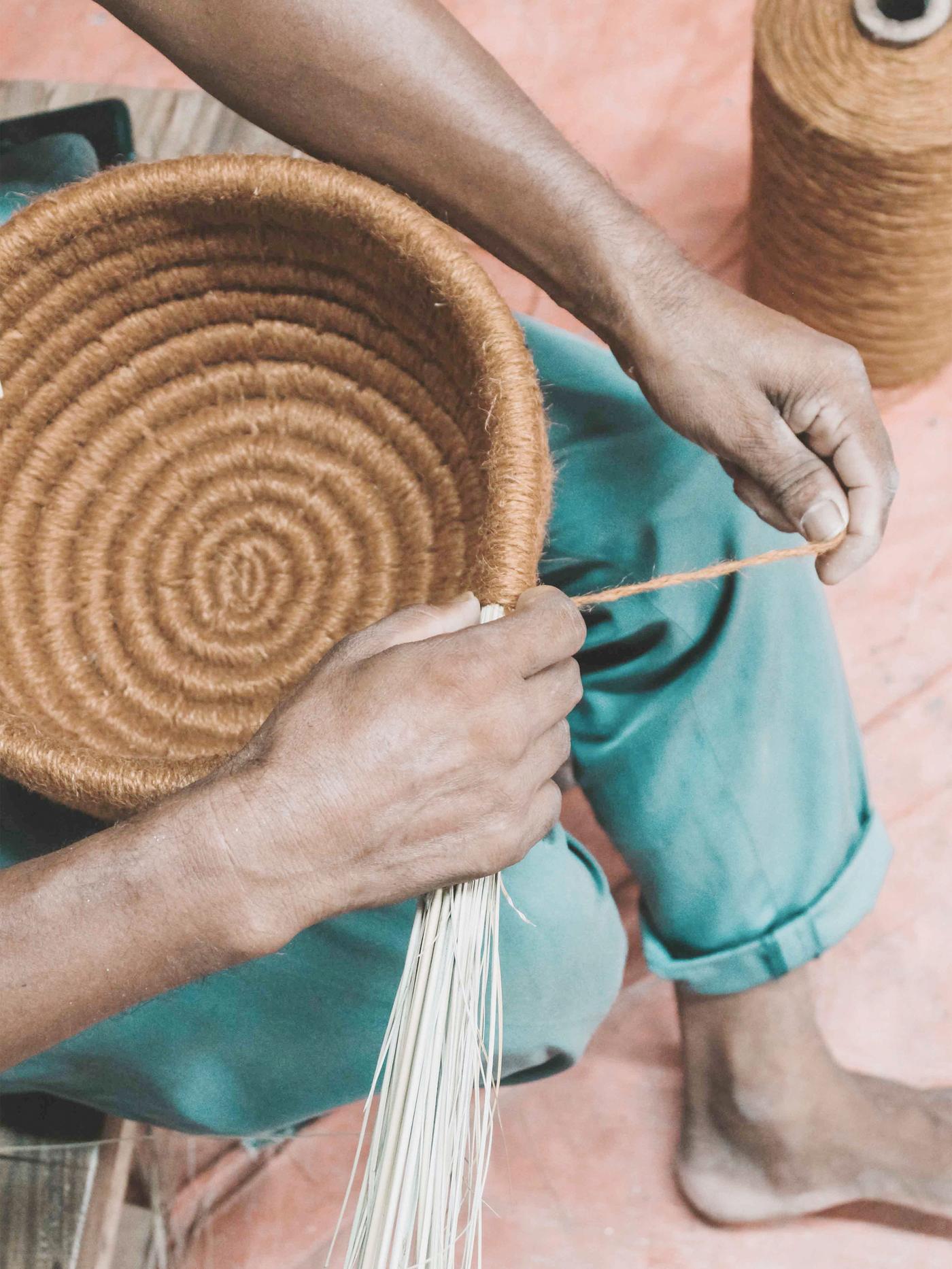 A person uses their hands to make a bowl from thick twine.