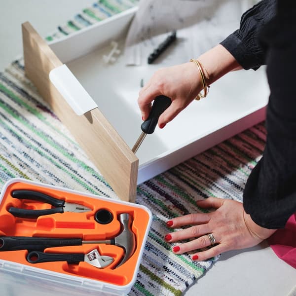 A person using a screwdriver to assemble a piece of furniture, with a toolbox in the foreground.