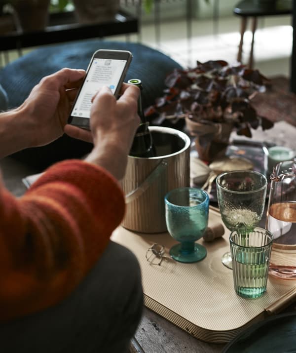 A person using their phone sitting in front of a coffee table with drinks.