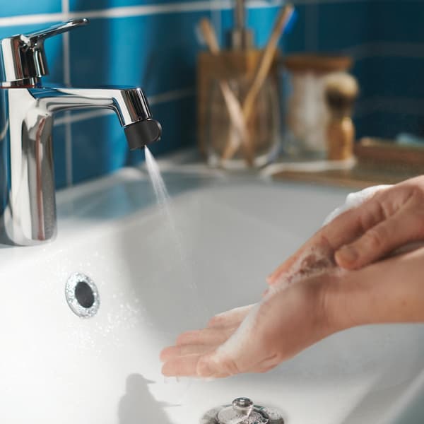 A person washing her hands with the bathroom tap, which is fixed with the ÅBÄCKEN nozzle in spray mode.