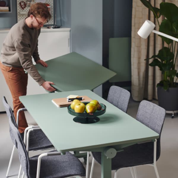 A person wearing a beige sweater and glasses is in the process of putting together a MITTZON foldable table in an office.