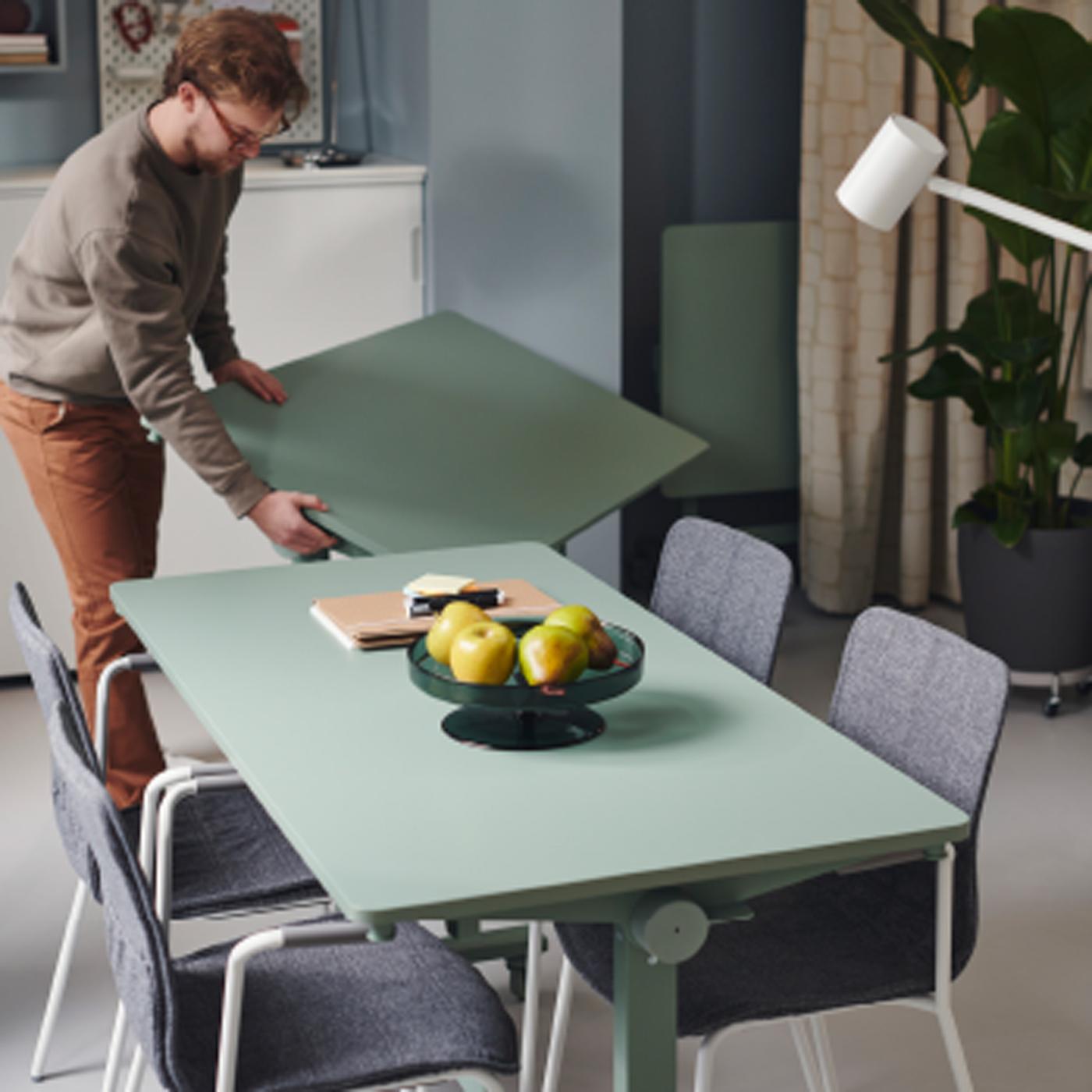 A person wearing a beige sweater and glasses is in the process of putting together a MITTZON foldable table in an office.
