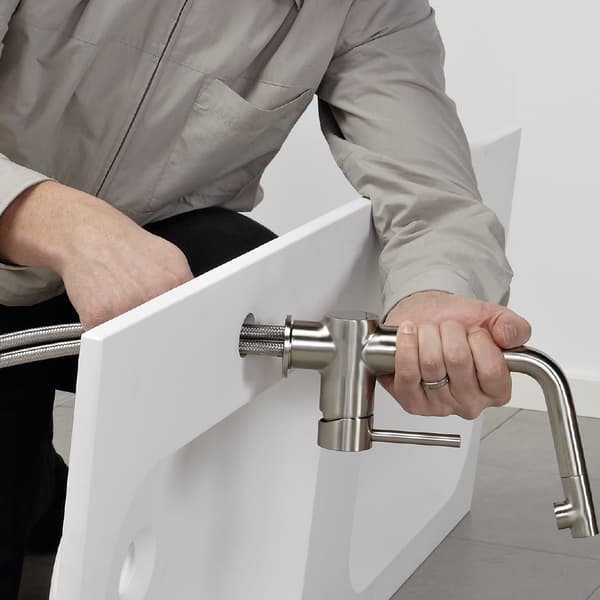 A person wearing a green t-shirt is fixing pipes under a sink with tools.