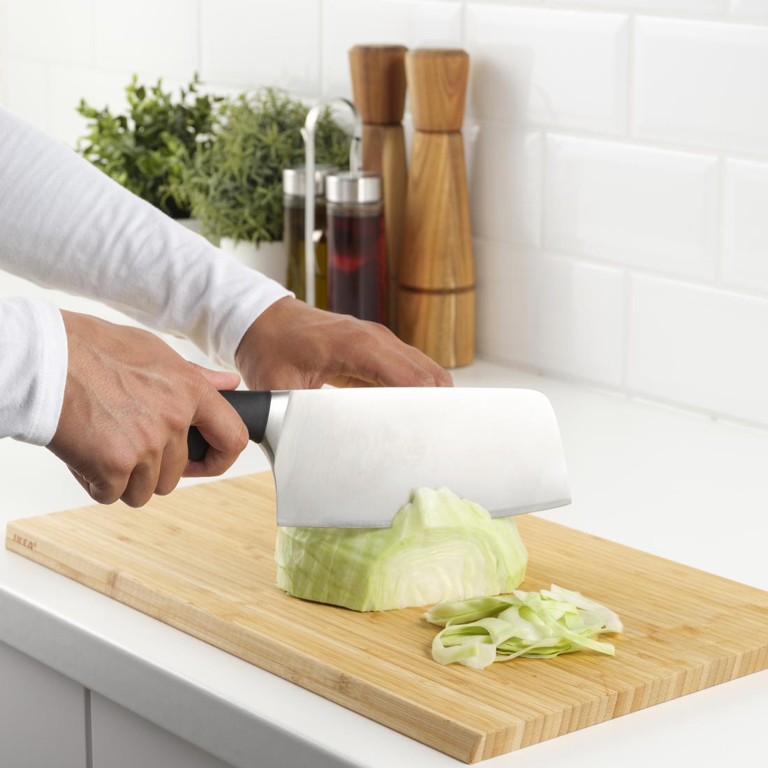 A person wearing a grey apron is chopping spring onions on a chopping board using a VÖRDA chinese chopper.