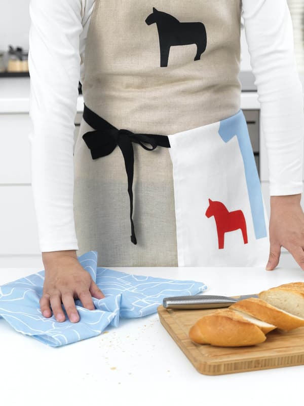 A person wearing a HÄSTHAGE apron and wiping the counter with a HÄSTHAGE tea towel.