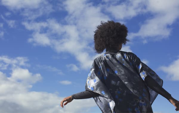 A person wearing a patterned black, blue and white kaftan standing against a blue sky.