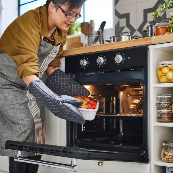 A person wears MARIATHERES oven gloves to remove food in an off-white POETISK oven dish from a MATTRADITION forced air oven.