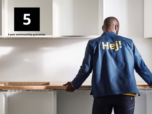 A person with a blue jacket with 'Hej' in yellow letters fitting a kitchen worktop