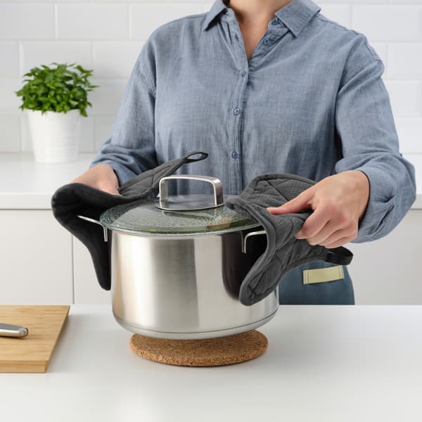 A person with a light blue shirt uses RINNIG pot holders hold sides of large pot and place it onto a cork trivet.