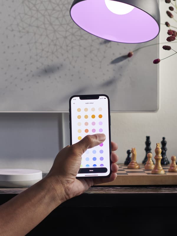 A person with a smart phone with IKEA app open pointing towards the lamp