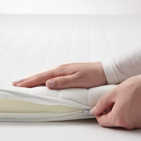 A person zipping up a white mattress topper.