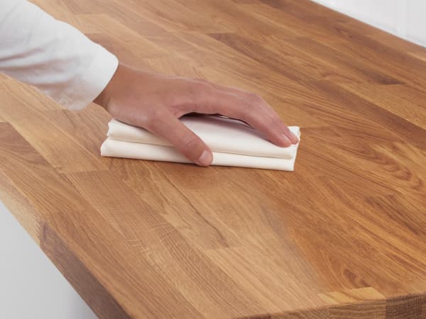 A person’s hand pressing down on a folded piece of paper on a wooden surface.