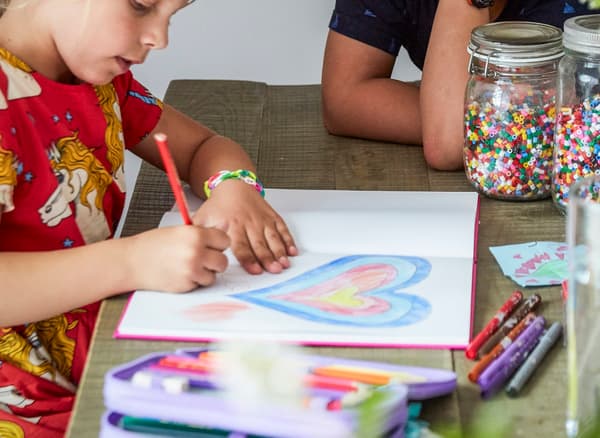A photo of two children sitting at a table drawing.