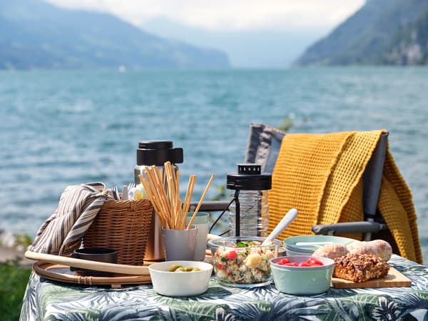 A picnic table covered in a jungle print table cloth, with various food containers filled with food