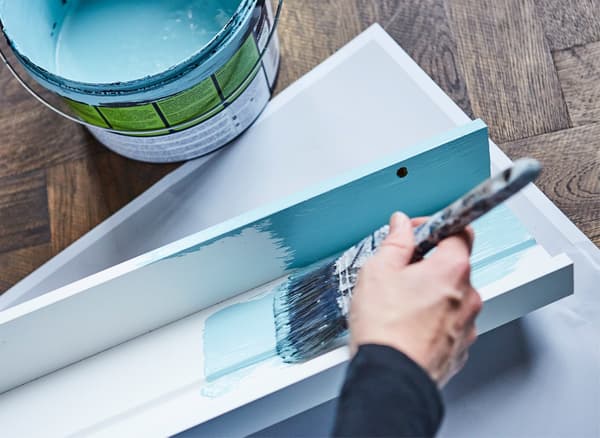 A picture ledge being painted in turquoise paint, to match a living room wall.
