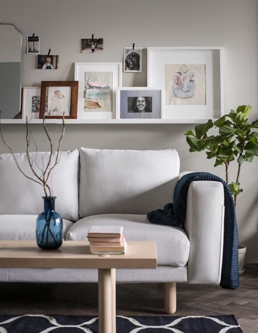 A picture ledge sits above a sofa and holds framed photos and artwork, while smaller photos are hung with decorative tape.