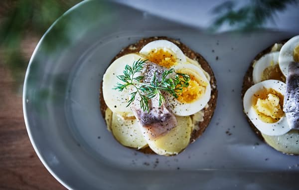 A piece of crispbread is topped with sliced potatoes, eggs and herring.