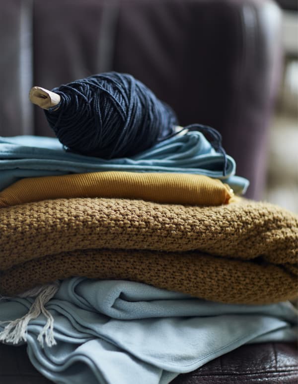 A pile of blankets and fabrics topped with a spool of wool.