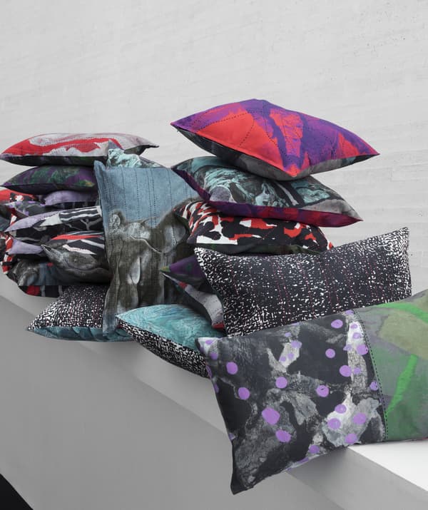 A pile of colourful and patterned cushions on a white shelf.