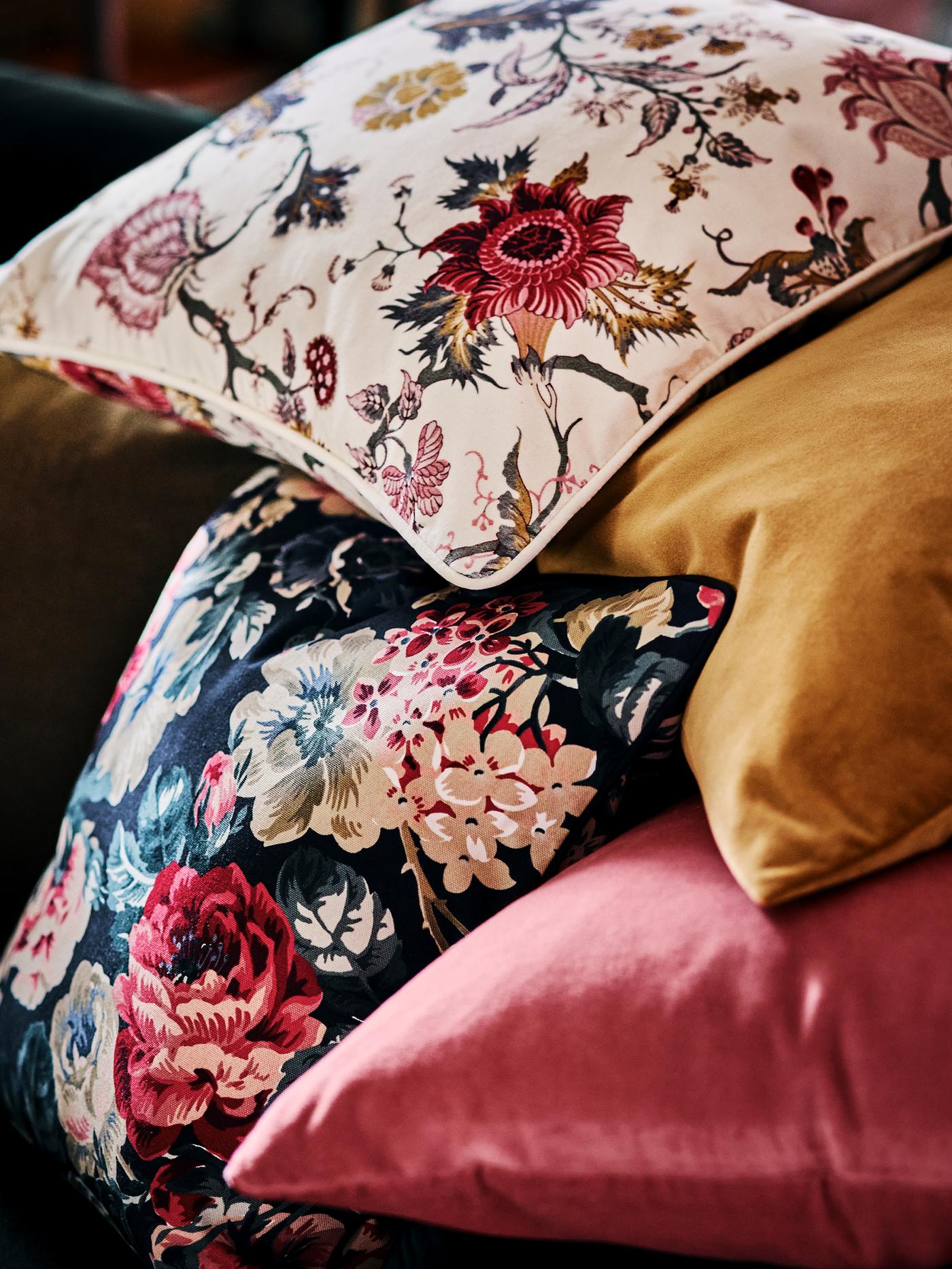 A pile of cushions made up of one LEIKNY cushion cover, one NÄSSELKLOCKA floral cusion cover, one pink and one brown-yellow.