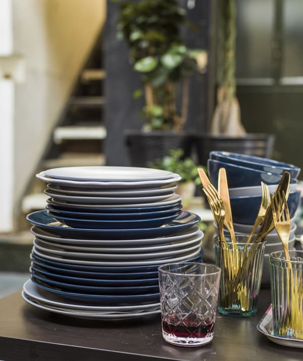 A pile of plates, cutlery and glasses on a table.