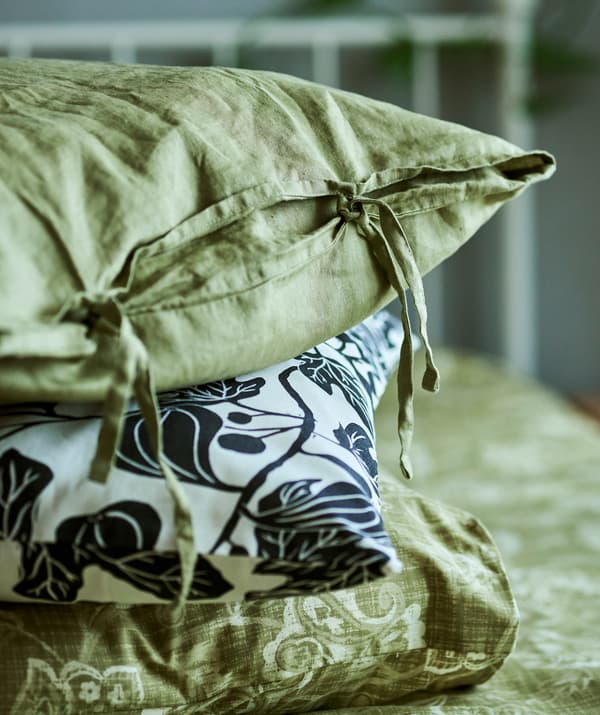 A pile of three pillows in different pillowcases – green linen with hand ties, a monochrome leaf pattern and green paisley.