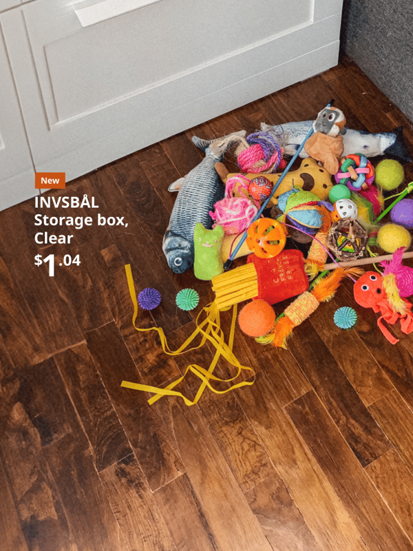 A pile of toys contained in an INVSBÅL Clear Storage box next to a white wardrobe and wooden floors
