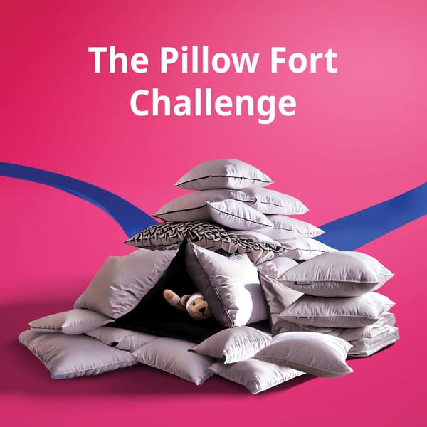 A pillow fort with a FABLER BJÖRN teddy bear soft toy hidding in the middle on a pink background with white text centralised at the top that reads 'The Pillow Fort Challenge'.